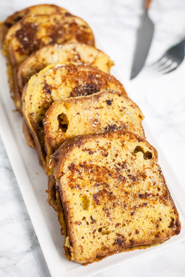 This Eggnog French Toast is a super easy breakfast recipe for Christmas morning and the holidays! Gluten free bread is soaked in a cinnamon egg mixture and then toasted until golden. It's topped with warm maple syrup and nutmeg. Everyone will love this French Toast! #breakfast #eggnog #christmas #glutenfree Eggnog French toast on white serving platter.