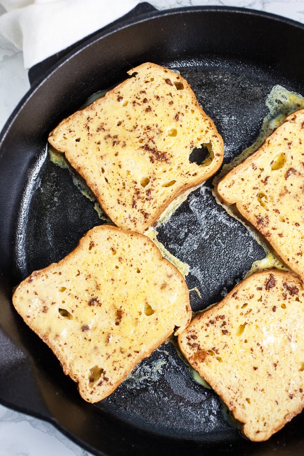 This Eggnog French Toast is a super easy breakfast recipe for Christmas morning and the holidays! Gluten free bread is soaked in a cinnamon egg mixture and then toasted until golden. It's topped with warm maple syrup and nutmeg. Everyone will love this French Toast! #breakfast #eggnog #christmas #glutenfree French toast frying in cast iron skillet.