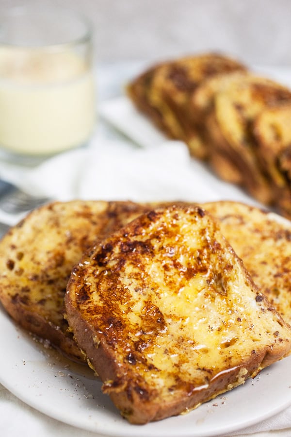 French toast with maple syrup on white plate with glass of eggnog.