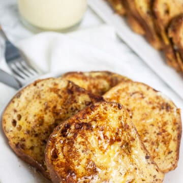 French toast on white plate with glass of eggnog.