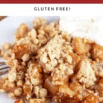 Gluten free apple crisp with whipped cream on white pate with fork.