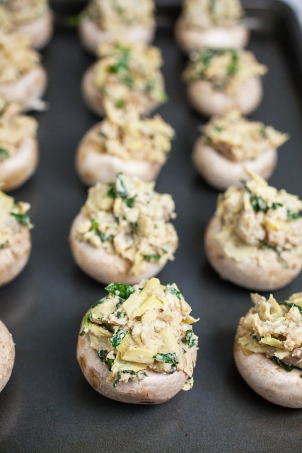 Uncooked stuffed mushrooms on metal baking sheet.