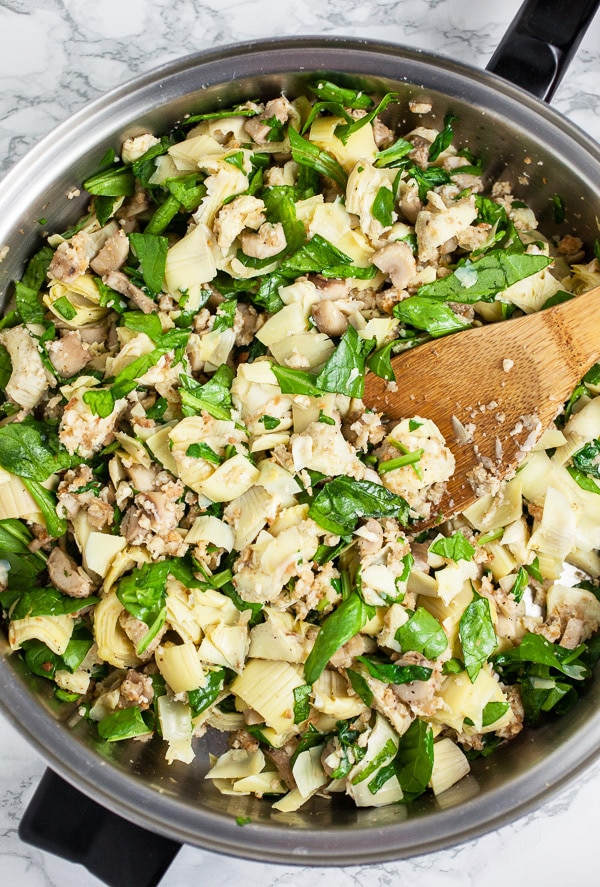 Spinach artichoke filling in skillet with wooden spoon.