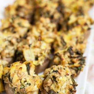 Spinach artichoke stuffed mushrooms on white serving platter.