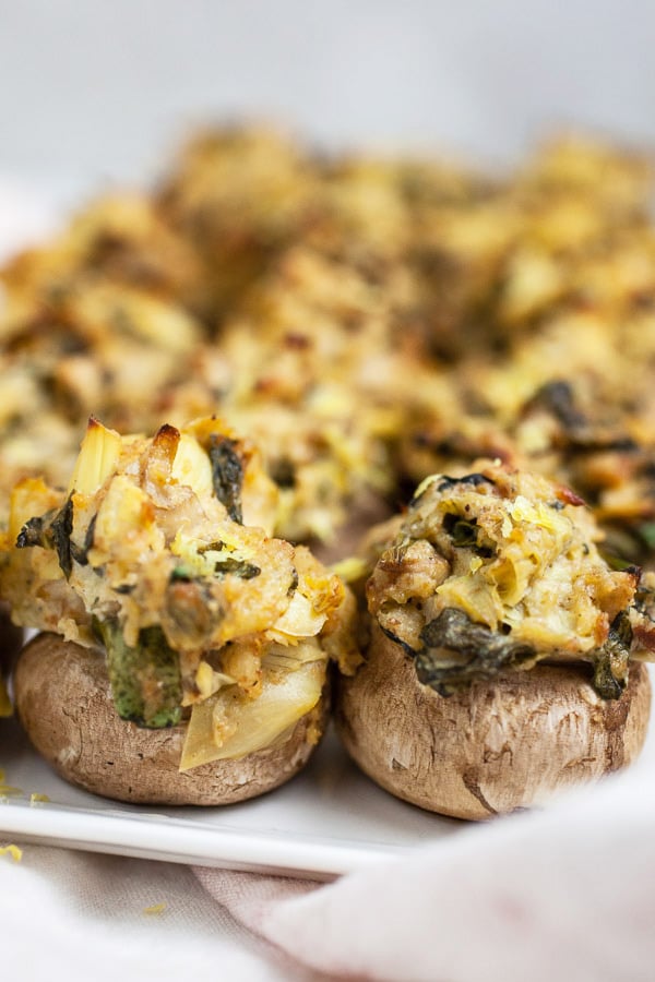 Spinach artichoke stuffed mushrooms on white serving platter.