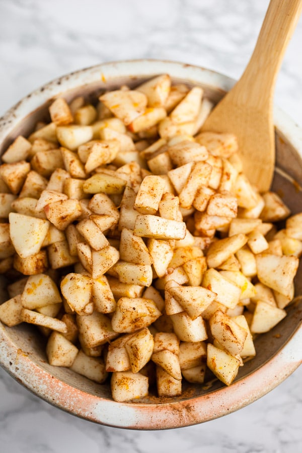 Peeled and diced apples with cinnamon in ceramic bowl with wooden spoon.