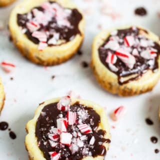 Peppermint chocolate cheesecake cups with crushed candy canes on white surface.