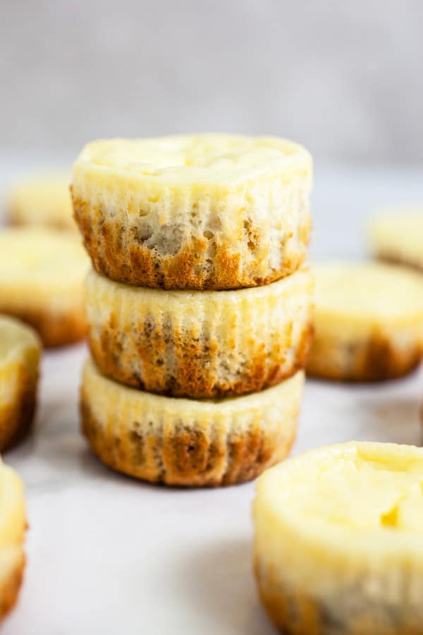Baked cheesecake cups stacked on white surface.