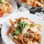 Cauliflower tomato penne pasta topped with Parmesan cheese, walnuts, and fresh basil on small white plates.