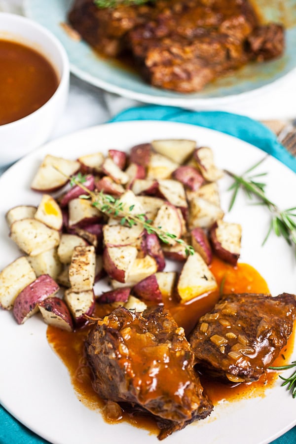 Pot roast with gravy, roasted potatoes, and rosemary on white plate.