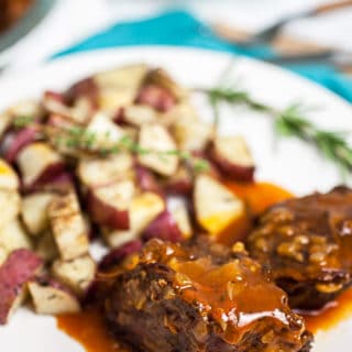 Beef pot roast with gravy, roasted potatoes, and rosemary on white plate.