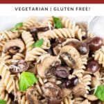 Mushroom olive pasta in white bowl with fork garnished with basil leaves.