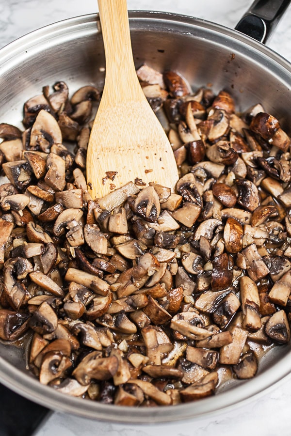 Chopped mushrooms sautéed in skillet with wooden spoon.