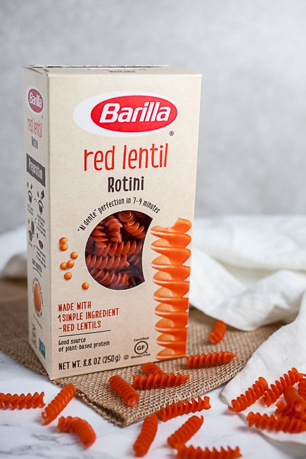 Box of red lentil rotini pasta on white surface.