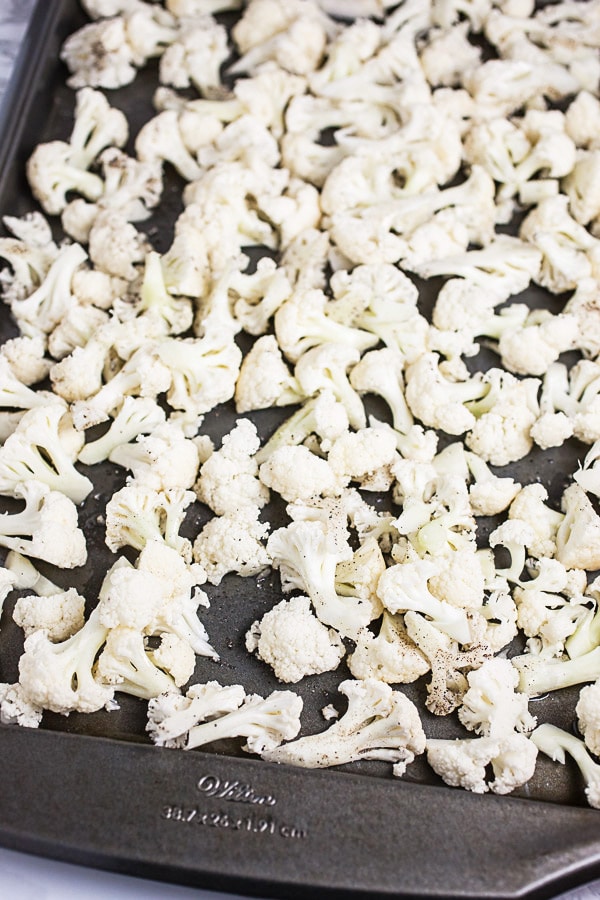 Uncooked cauliflower florets tossed in olive oil, salt, and pepper on baking sheet.