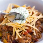 Slow Cooker No Bean Chili With Sour Cream and Shredded Cheese In White Bowl