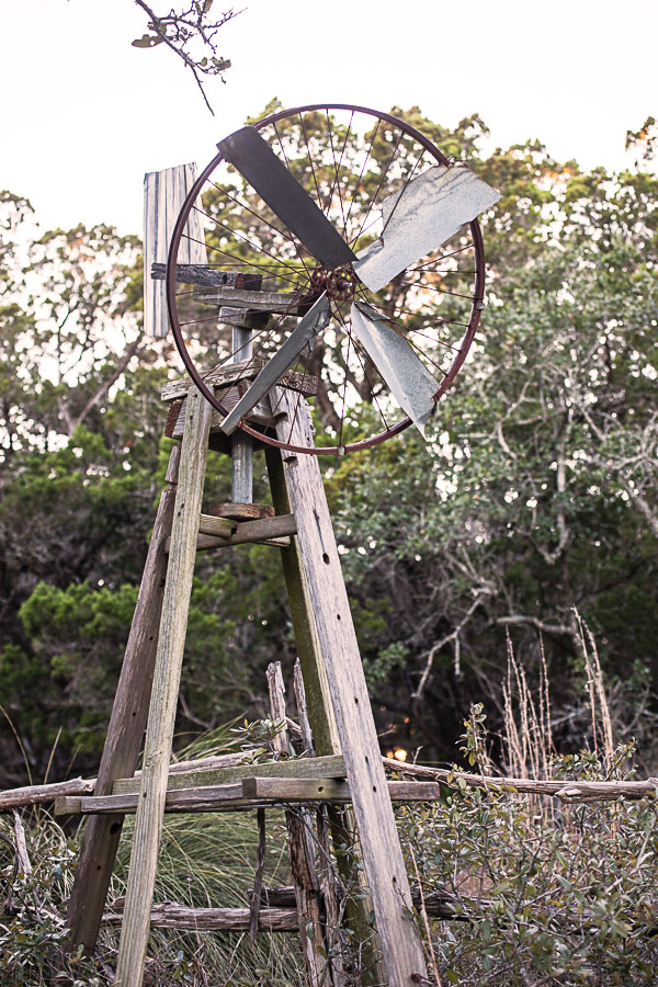 Old wooden windmill in front of trees.