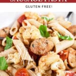 Cauliflower, chicken sausage, and tomato penne pasta with fresh basil in white bowl.