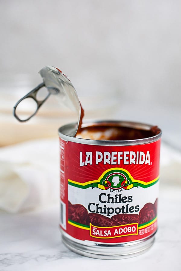Opened can of chipotle peppers in adobo sauce on white surface.
