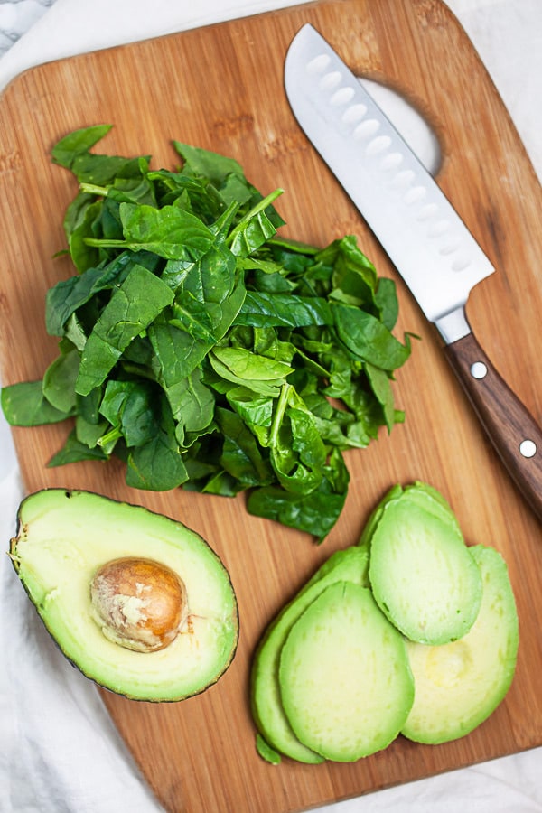 Sliced avocado and spinach on wooden cutting board with knife.