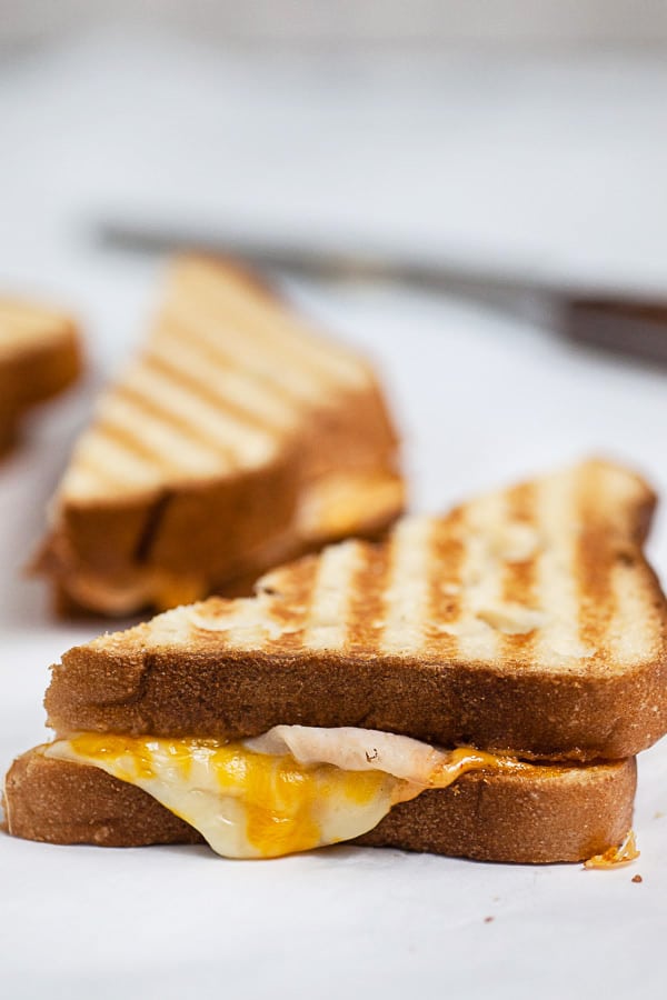 Toasted chicken panini sandwich cut in half on white surface.