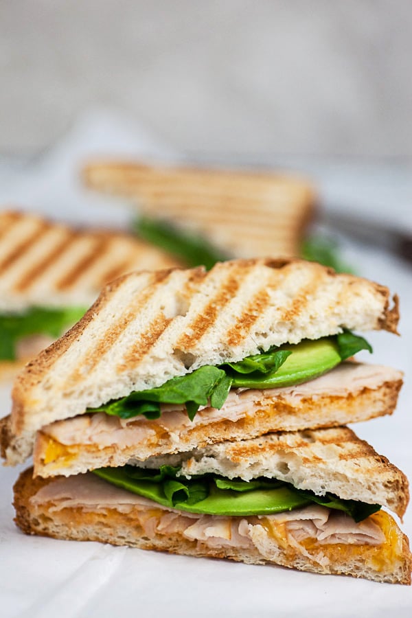 Chipotle chicken panini with avocado and spinach cut in half and stacked on white surface.
