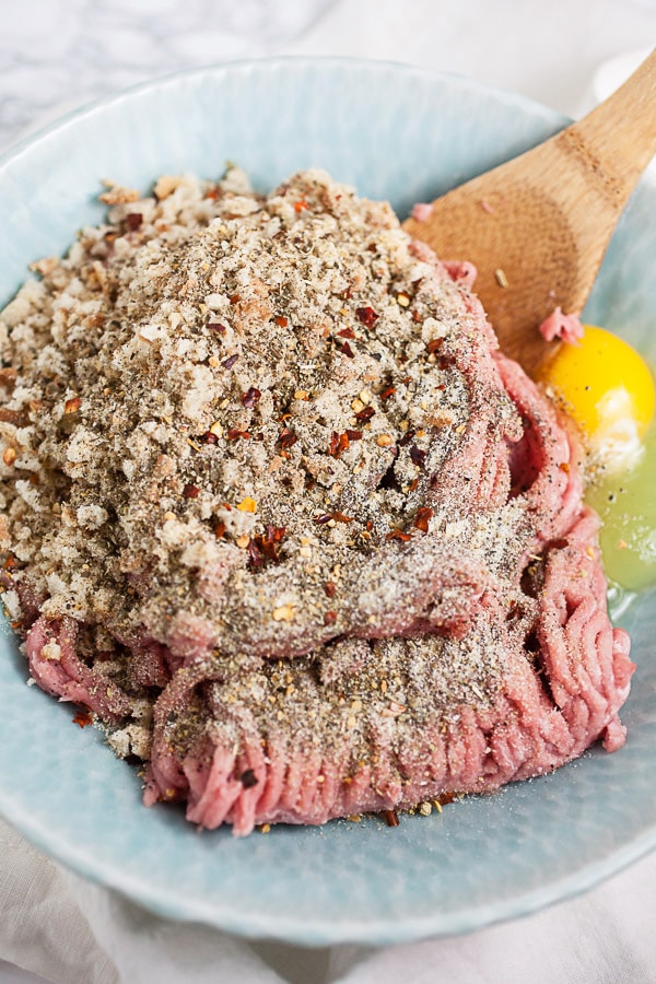 Ground turkey, Panko breadcrumbs, spices, and eggs in blue bowl with wooden spoon.