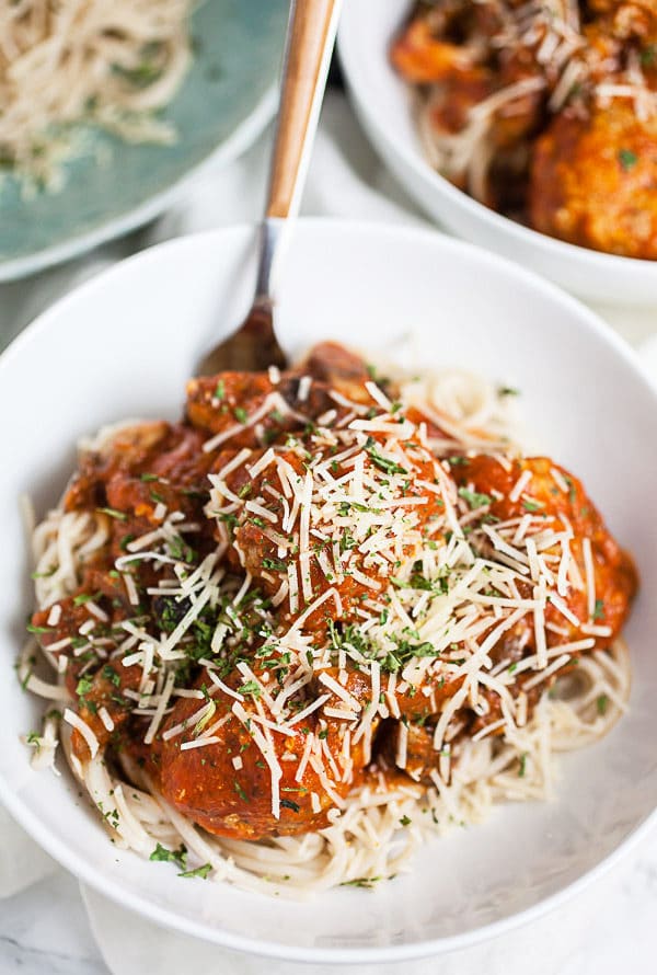 Meatballs in marinara sauce over spaghetti noodles and topped with Parmesan cheese in white bowl.