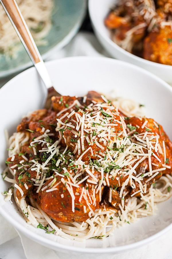 Turkey meatballs in marinara sauce over spaghetti noodles and topped with Parmesan cheese in white bowl.