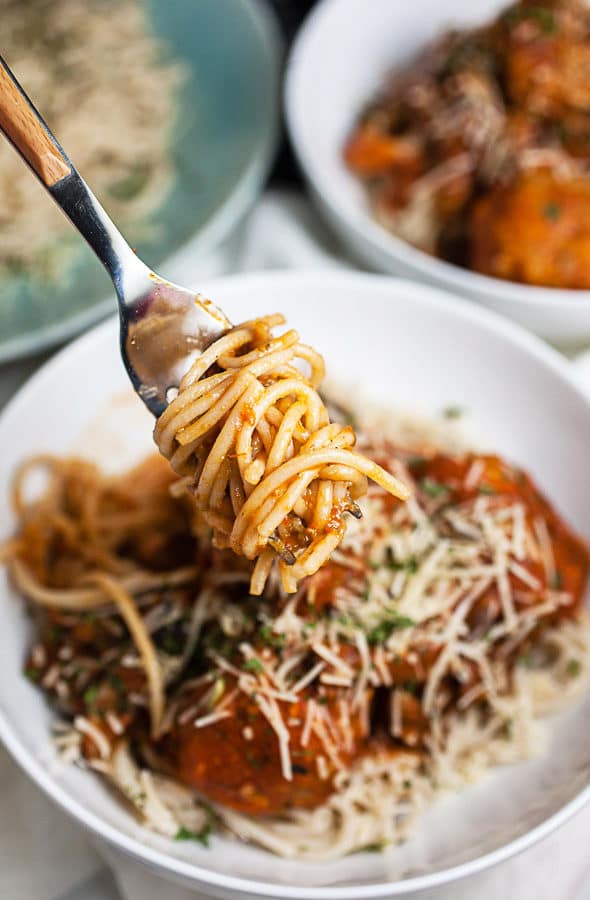 Spaghetti noodles on fork lifted from white bowl of meatballs and marinara sauce.