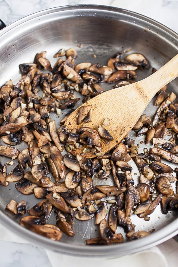 Mushrooms sautéed in skillet with wooden spoon. 