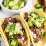 Pork carnitas tacos on corn tortillas with guacamole, cilantro, and sliced jalapenos.