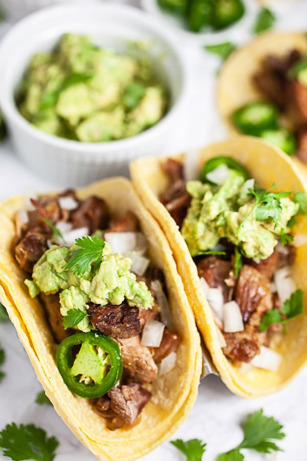 Pork carnitas tacos on corn tortillas with guacamole, cilantro, and sliced jalapenos.