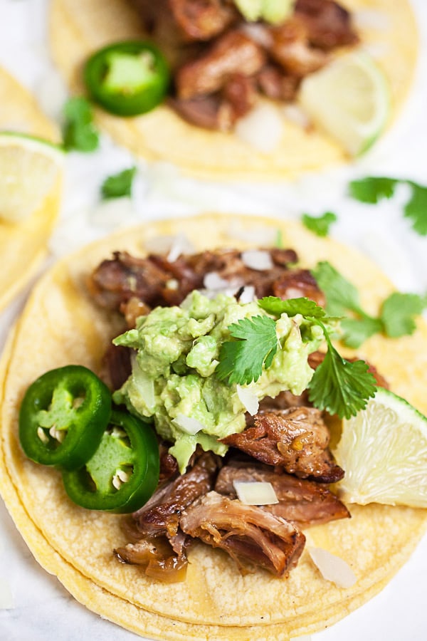 Pork carnitas tacos on corn tortillas with guacamole, cilantro, jalapeno peppers, and limes.