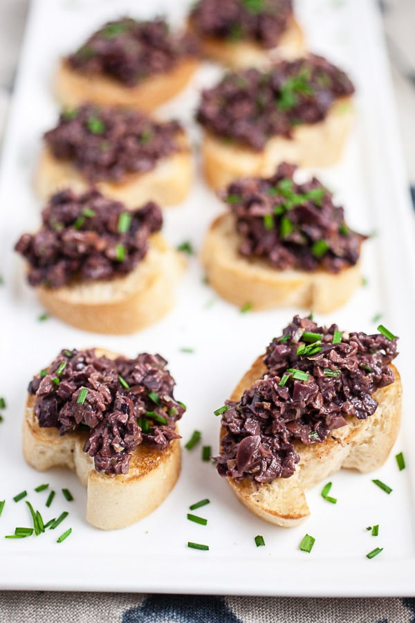 Kalamata olive tapenade on crostini on white serving platter.