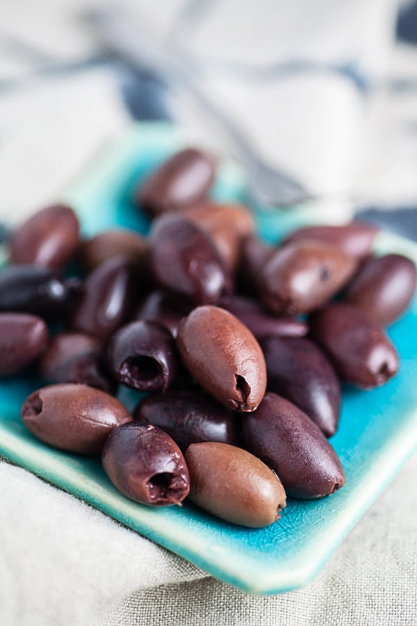 Whole Kalamata olives on small blue serving dish.