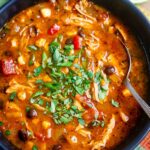 Chicken enchilada soup in bowl with spoon garnished with fresh cilantro.