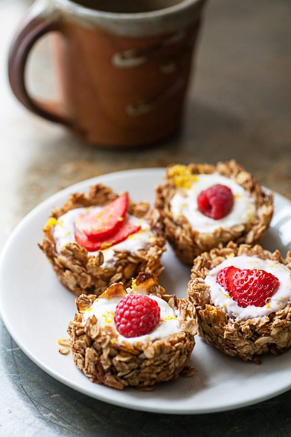 #ad These Greek Yogurt Oatmeal Cups are the perfect easy and healthy breakfast recipe! The oats are mixed with coconut oil, lemon zest, and cinnamon and then baked until crispy. They're filled with yogurt that's creamy and lightly sweetened with honey. Great for a brunch, dessert, or to serve at a party! @GreekGodsYogurt #oatmeal #yogurt #cups #healthy #glutenfree Oatmeal yogurt cups on small white plate with cup of coffee.