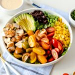 Grilled Southwest chicken salad in white bowl with tomatoes, corn, greens, and sliced avocado.