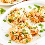 Mexican street corn tacos on white platter garnished with fresh cilantro.