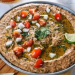 Mexican black beans hummus in bowl garnished with tomatoes, onions, cilantro, and lime wedge.