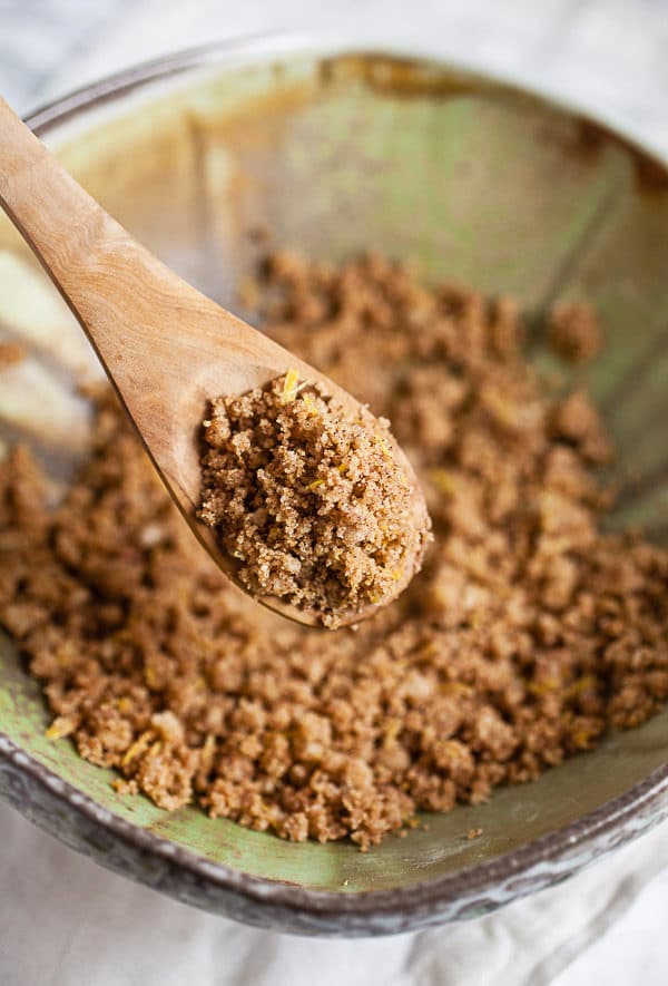 Spoonful of cinnamon streusel topping lifted from green ceramic bowl.