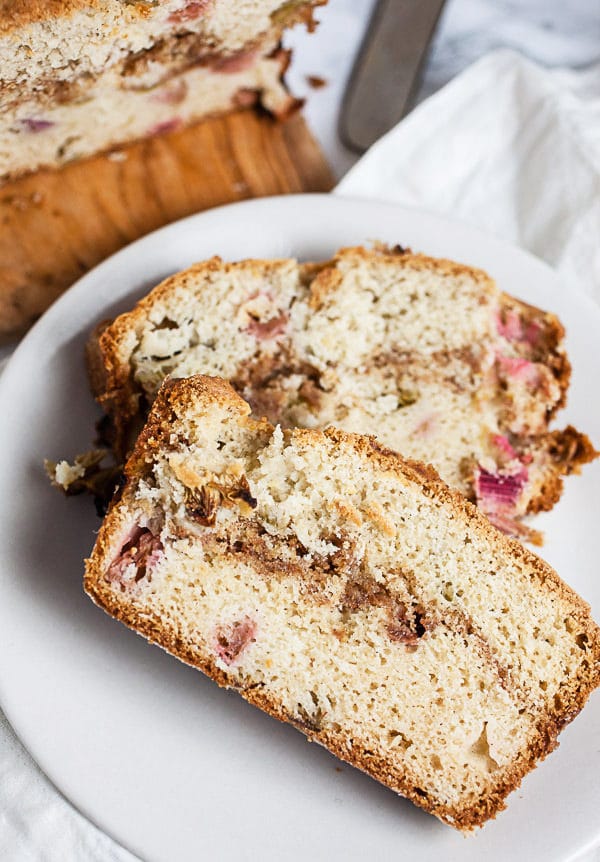 This Old Fashioned Rhubarb Bread is easy to make and totally delicious! It's made with sour cream so it's super moist. A layer of cinnamon streusel is baked into the middle of the bread giving it great crunch and texture. Perfect for breakfast, brunch, or dessert! This recipe is gluten free as well. A great way to welcome the spring and summer season! #rhubarb #bread #breakfast #streusel #glutenfree Slices of gluten free rhubarb bread on small white plate.