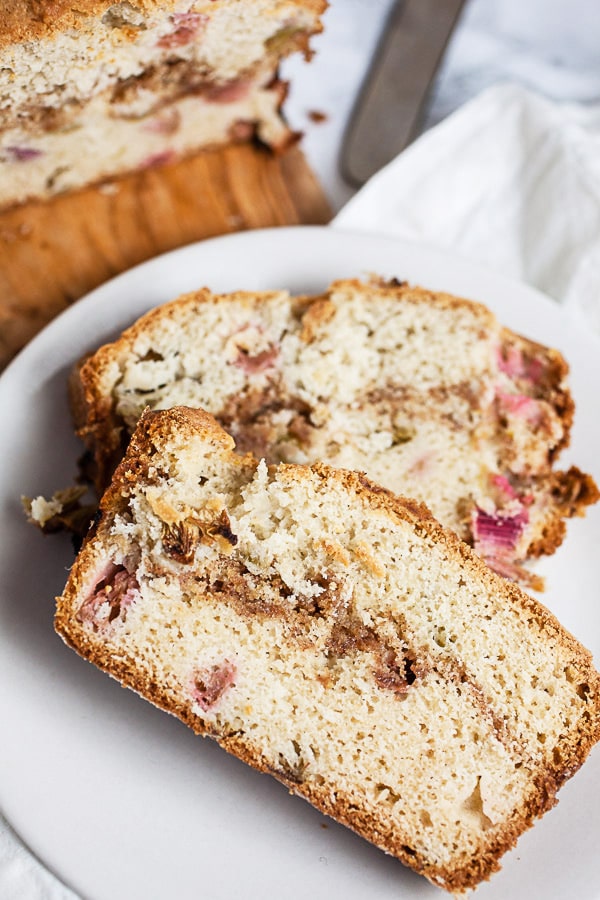 This Old Fashioned Rhubarb Bread is easy to make and totally delicious! It's made with sour cream so it's super moist. A layer of cinnamon streusel is baked into the middle of the bread giving it great crunch and texture. Perfect for breakfast, brunch, or dessert! This recipe is gluten free as well. A great way to welcome the spring and summer season! #rhubarb #bread #breakfast #streusel #glutenfree Slices of rhubarb bread with streusel on small white plate.