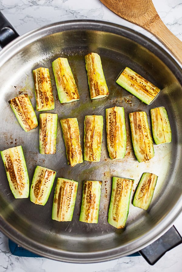 Zucchini wedges sautéed in skillet.