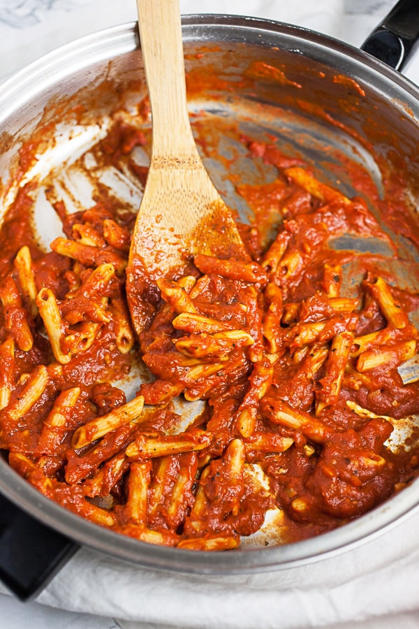 This Skillet Zucchini Parmesan recipe makes the perfect easy and healthy weeknight dinner for one! The pasta is cooked in a rich tomato sauce, combined with fresh zucchini, and then baked in the oven. It's topped with mozzarella and Parmesan cheese. This meal is vegetarian and gluten free! #pasta #zucchini #skillet #vegetarian #glutenfree Penne noodles cooked in marinara sauce in skillet.