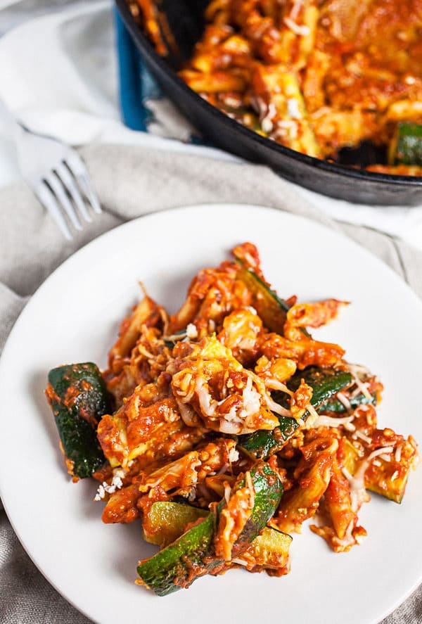 This Skillet Zucchini Parmesan recipe makes the perfect easy and healthy weeknight dinner for one! The pasta is cooked in a rich tomato sauce, combined with fresh zucchini, and then baked in the oven. It's topped with mozzarella and Parmesan cheese. This meal is vegetarian and gluten free! #pasta #zucchini #skillet #vegetarian #glutenfree Skillet zucchini Parmesan with marinara sauce on small white plate.