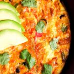 Southwestern frittata in skillet garnished with avocado slices.
