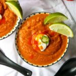 Southwestern pumpkin soup in bowls garnished with sour cream, sliced jalapeno, and lime wedges.