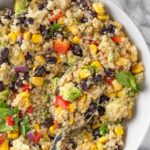 Southwest quinoa salad with black beans, corn, bell peppers, and avocado in white bowl with spoon.